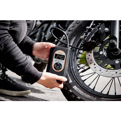 Eine Person überprüft den Reifendruck eines Motorrads mit einem digitalen Druckmesser, der 2,4 bar anzeigt.