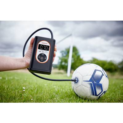 Eine Hand hält eine elektrische Luftpumpe, die einen Fußball auf einem Spielfeld aufpumpt. Im Hintergrund ist ein Tor zu sehen.