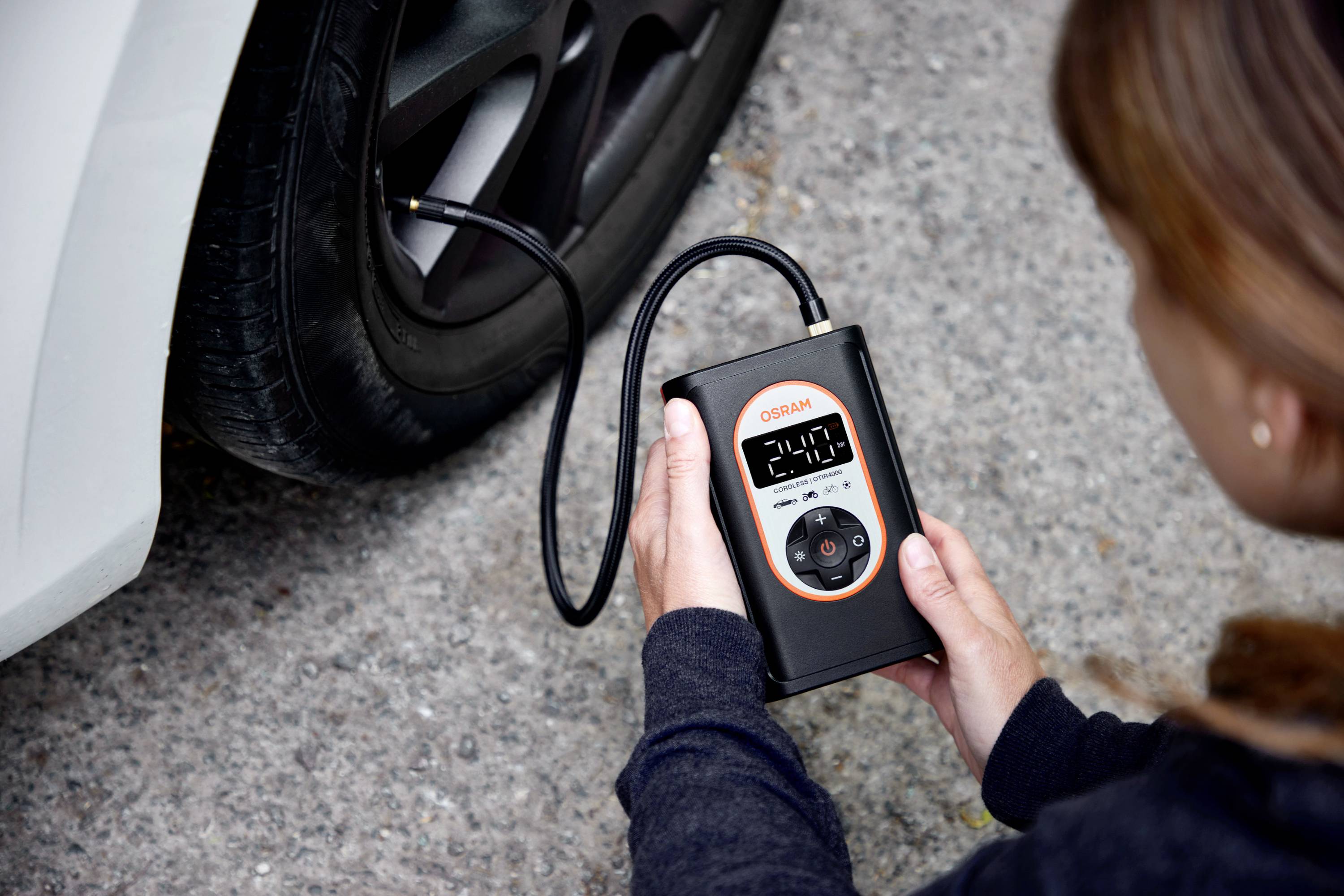 Person prüft den Reifendruck eines Autos mit einem digitalen Reifendruckmesser. Gerät zeigt 2,00 bar an.