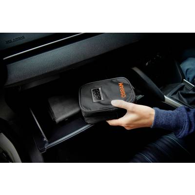 Hand legt eine schwarze Tasche mit 'OSRAM'-Logo in ein geöffnete Handschuhfach im Auto.