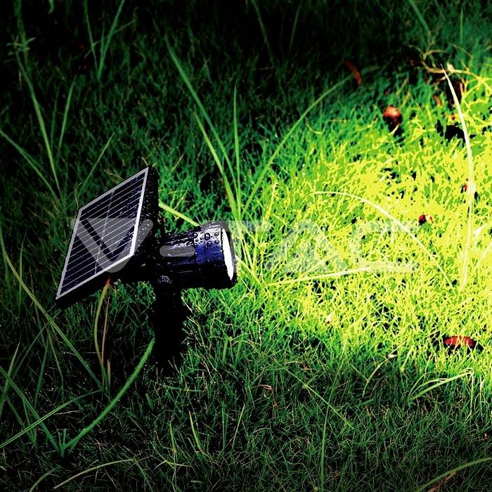 Eine solarbetriebene Lampe erleuchtet nachts grünes Gras und hebt Grashalme und Wassertropfen in ihrem Lichtstrahl hervor.