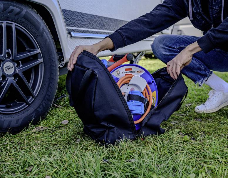 Eine Person packt Kabelzubehör in eine schwarze Tasche neben einem Auto auf einer Grasfläche ein.
