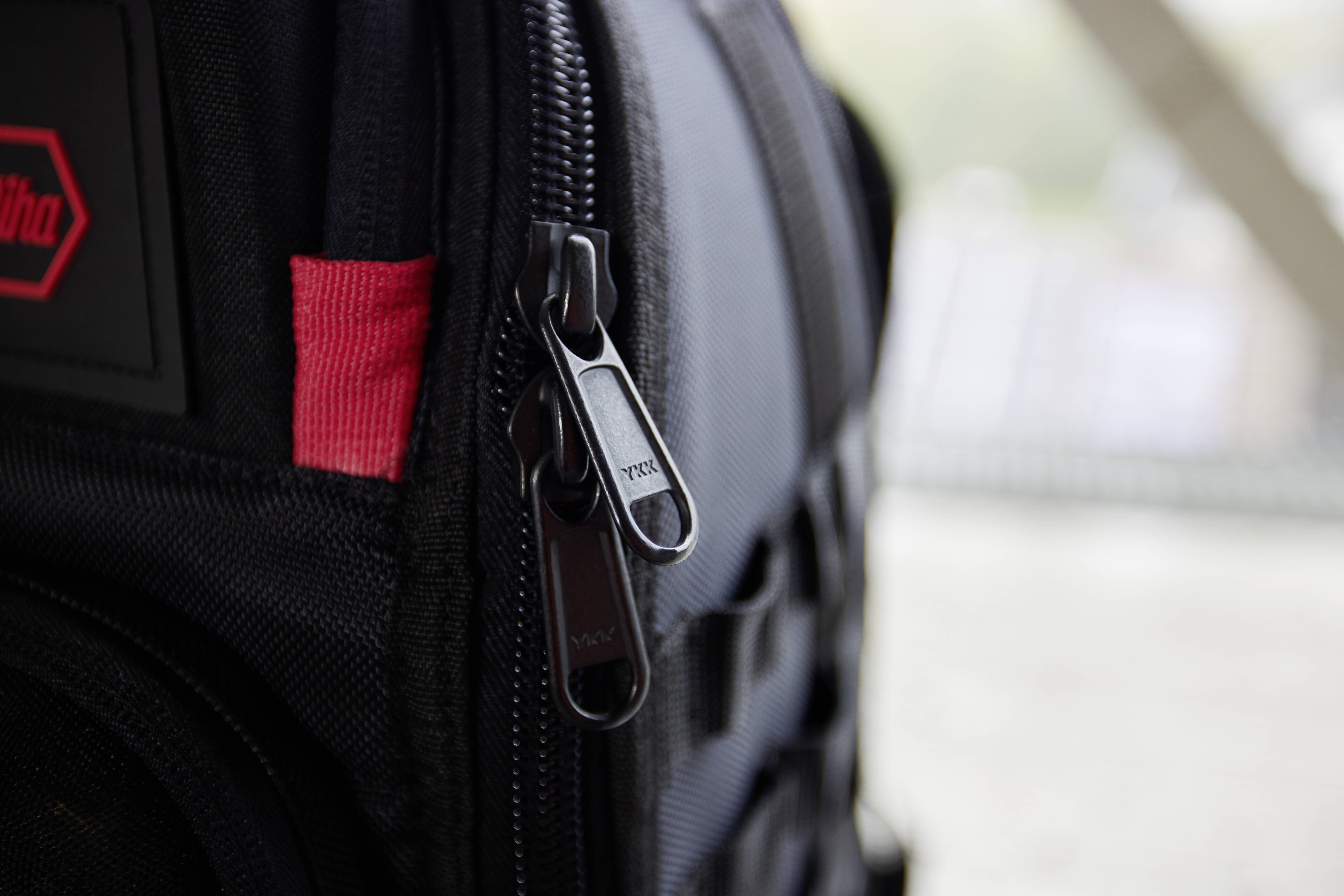 Ein schwarzer Rucksack mit roten Akzenten und einem offenen Reißverschluss, der den oberen Teil zeigt. Nur ein Teil des Rucksacks ist sichtbar.