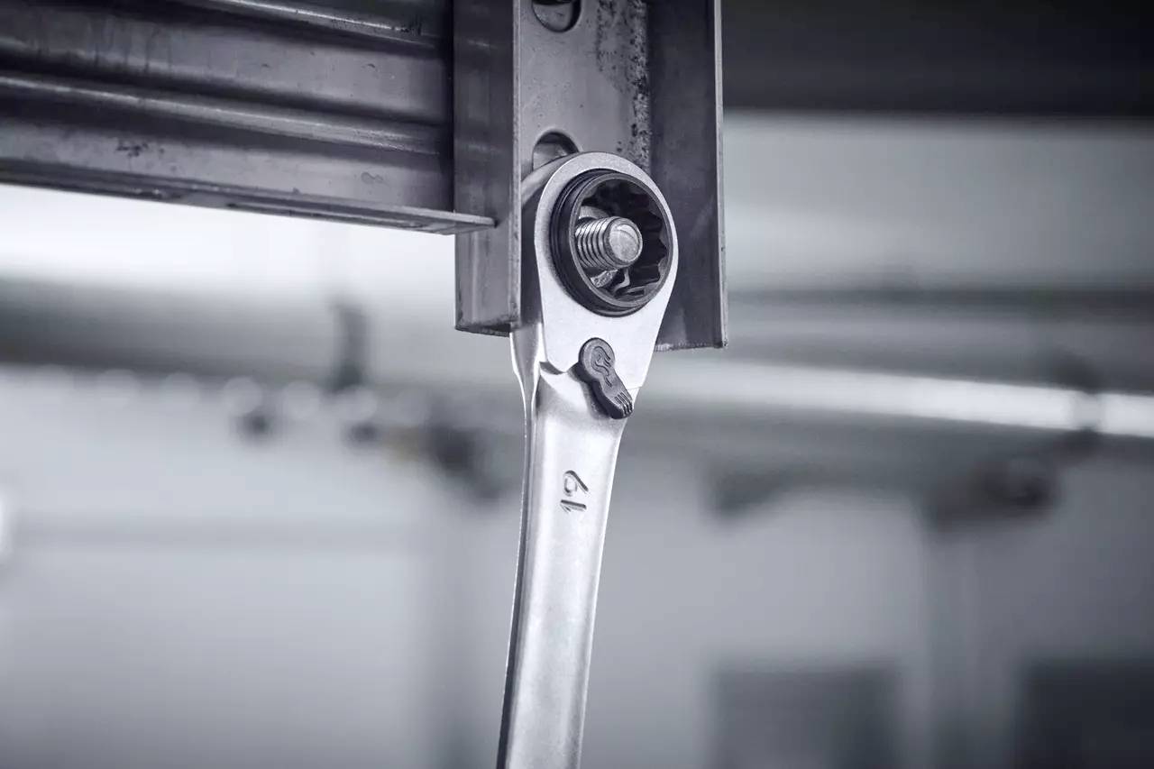 Ein Schraubenschlüssel zieht an einer Schraube in einer Metallstruktur, Symbol für Wartung oder Reparaturarbeiten in einer Werkstatt.