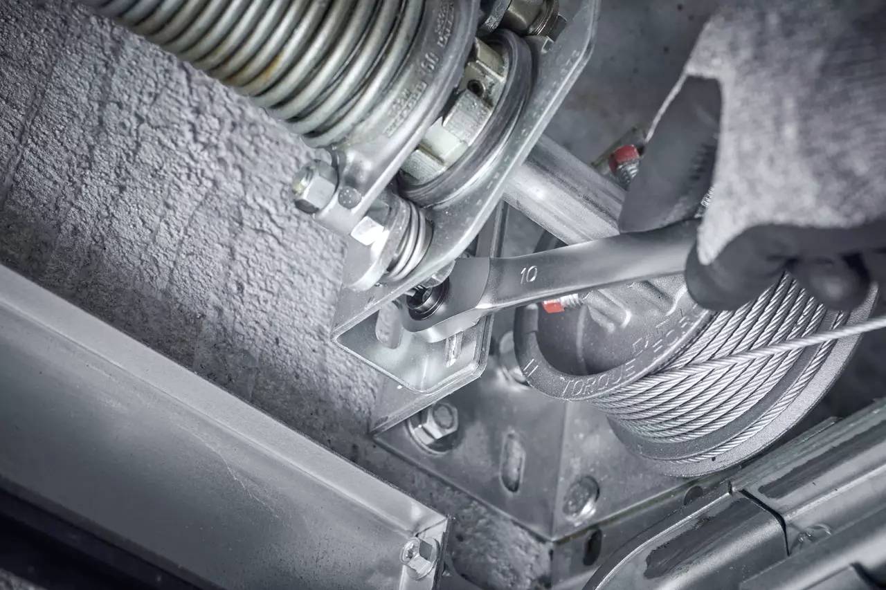 Eine Hand mit Arbeitshandschuh benutzt einen Schraubenschlüssel, um eine Schraube an einer Metallstruktur zu befestigen.