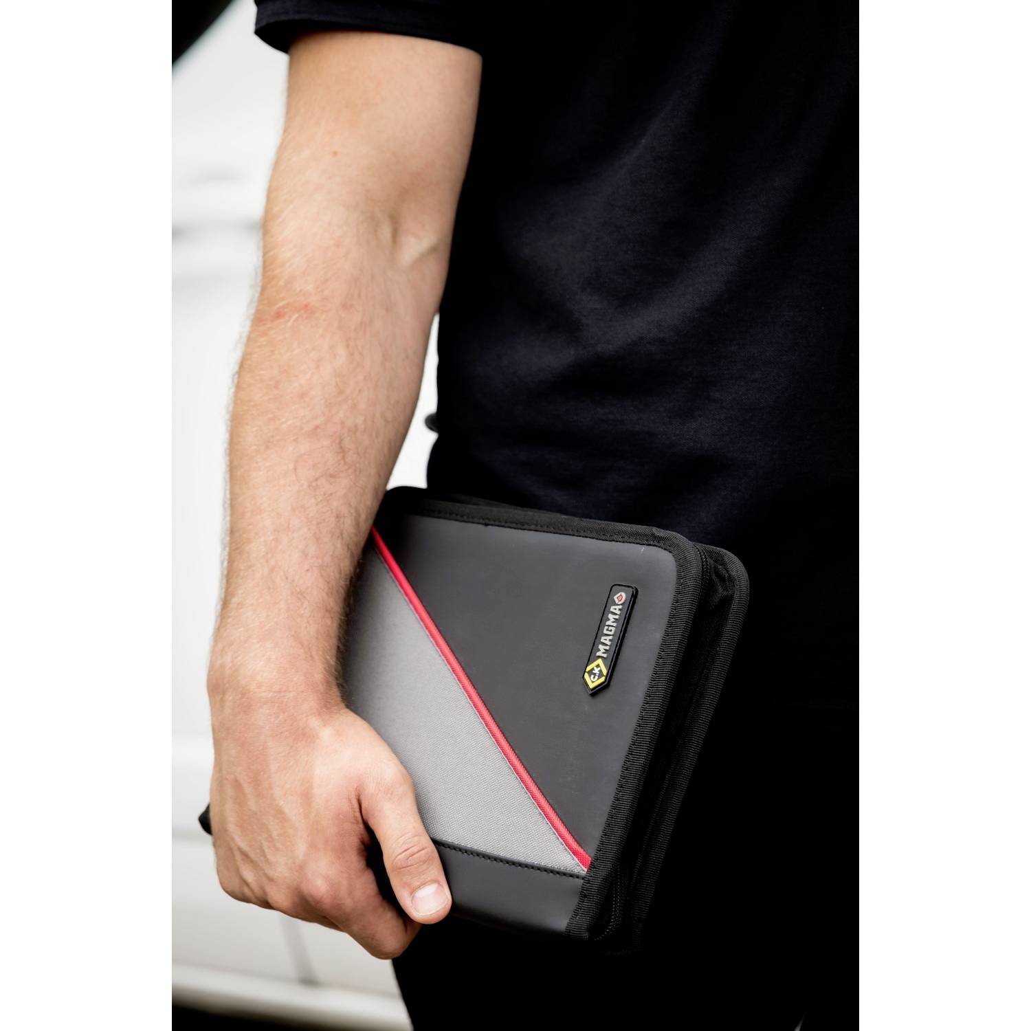 Ein Mann hält eine schwarze Tasche mit rotem und grauem Muster in der Hand. Die Tasche hat ein gelbes Logo.