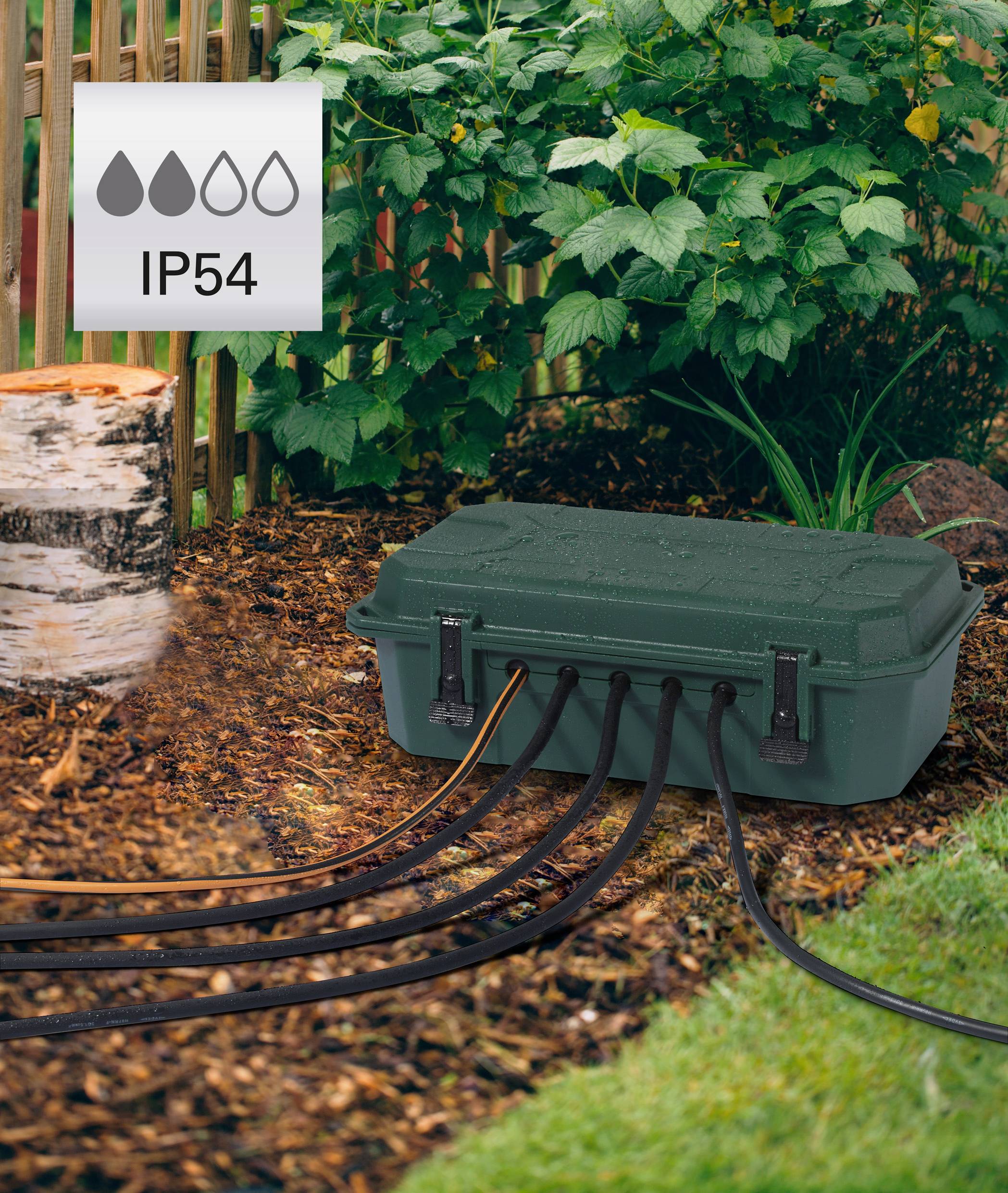 Eine grüne Schutzbox mit mehreren Kabeln liegt im Garten vor einem Holzzaun. Ein Symbol zeigt 'IP54', was auf Wasserschutz hinweist.