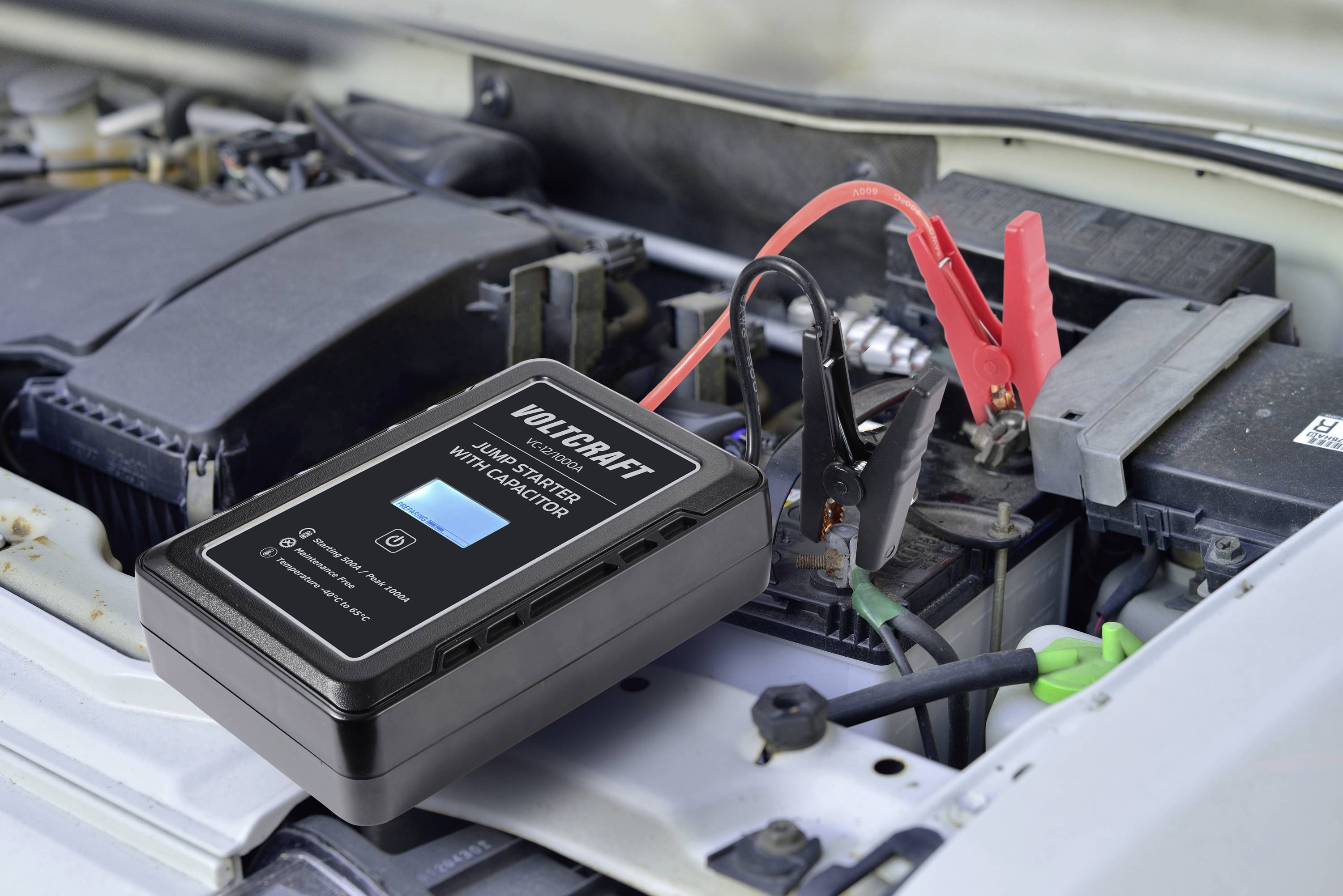 Ein Ladegerät ist an eine Autobatterie angeschlossen. Das Gerät zeigt einen Ladevorgang an. Im Hintergrund ist der Motorraum sichtbar.