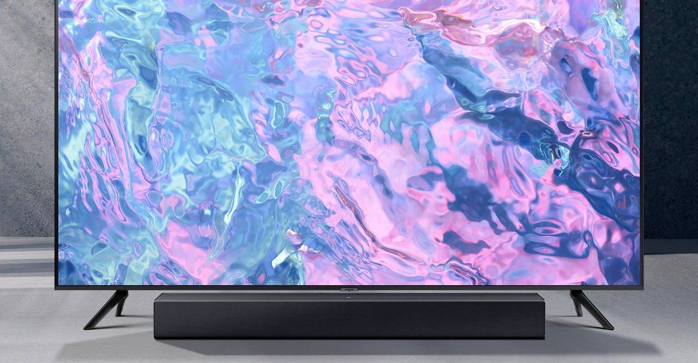 Ein moderner Fernseher steht auf einem Tisch. Auf dem Bildschirm sind abstrakte, bunte Wasserwellen in Blau- und Rosatönen zu sehen.