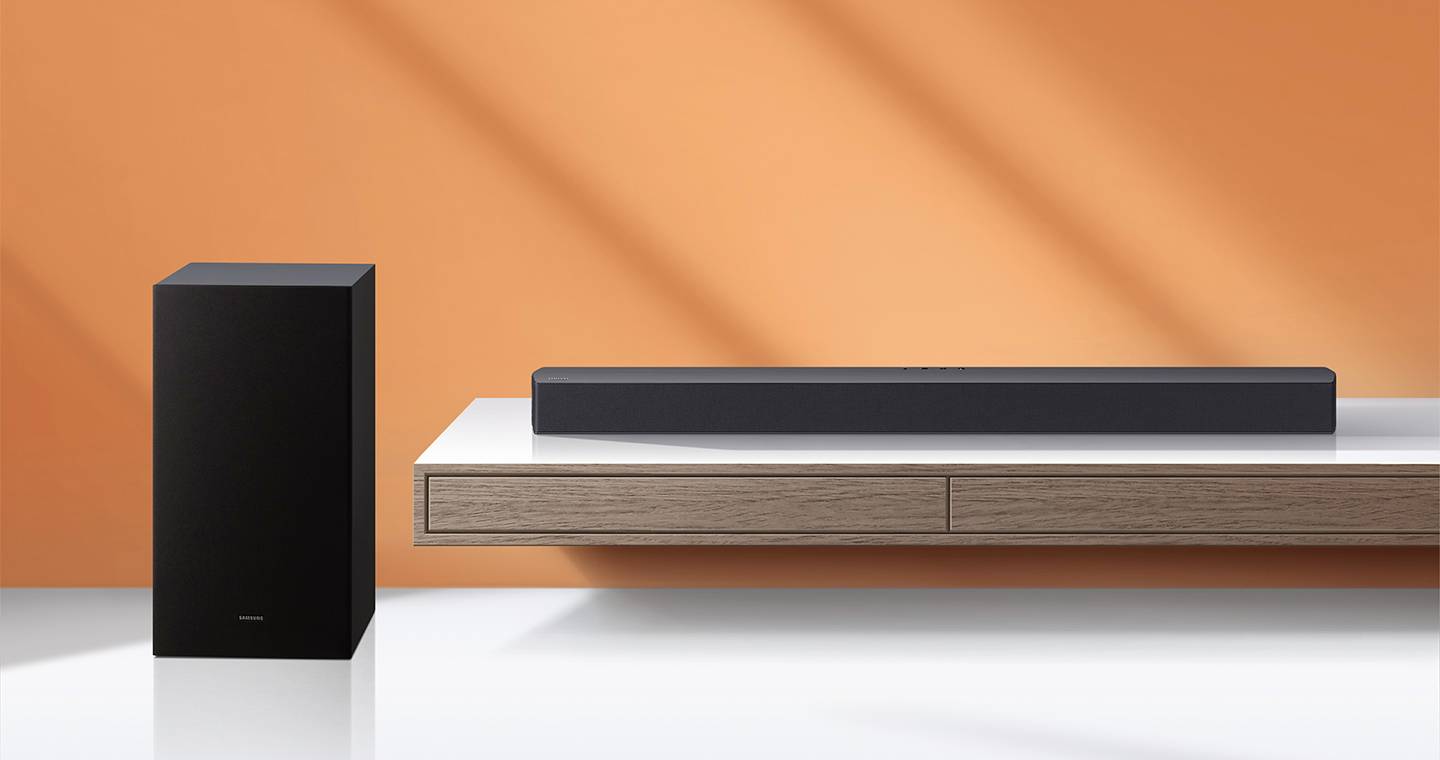 Schwarzer Lautsprecher und Soundbar auf einem Holztisch vor einer orangefarbenen Wand. Modernes, minimalistisches Design.