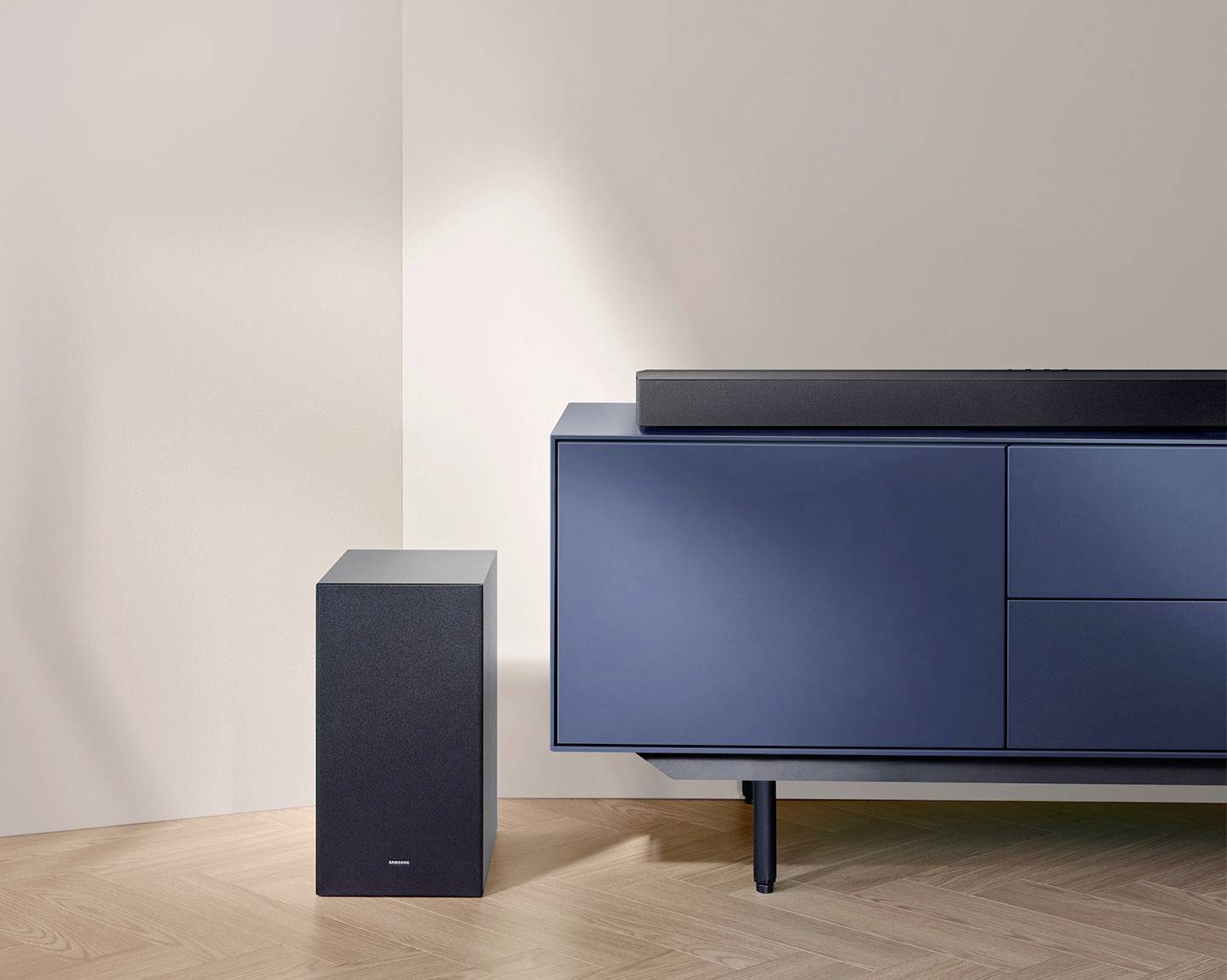 Blaue Kommode mit schwarzem Lautsprecher und Subwoofer auf Holzboden in modernem, minimalistischem Raum.