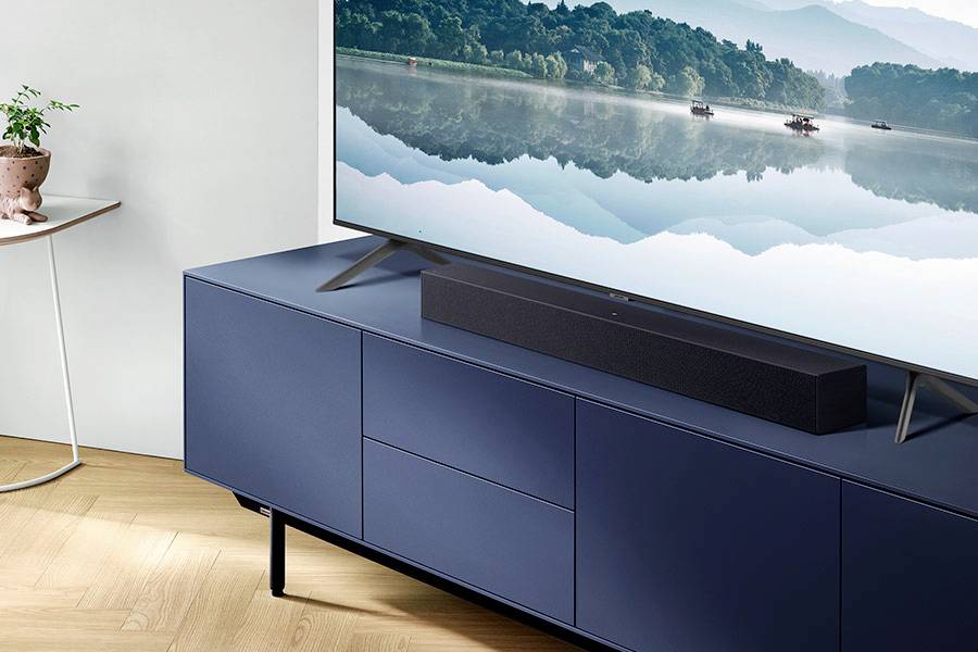 Ein moderner Fernseher auf einem blauen Schrank zeigt eine Landschaft mit einem ruhigen See und Bergen im Hintergrund.