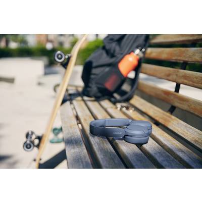 Kopfhörer auf einer Parkbank, daneben ein Skateboard und ein schwarzer Rucksack mit einer roten Wasserflasche. Outdoor-Szene.