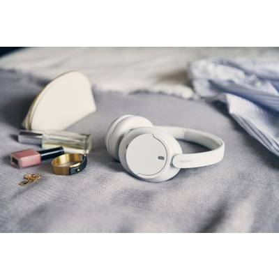 Weiße Kopfhörer auf einer grauen Decke, umgeben von Parfüm, Lippenstift, Creme, Ring und einem Schlüssel. Möglichkeit zur Entspannung.