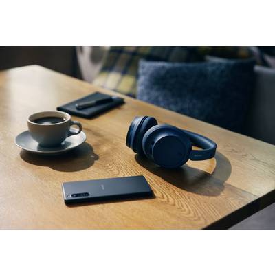 Smartphone, Kopfhörer und Kaffeetasse auf Holztisch; ruhige Arbeitsumgebung.
