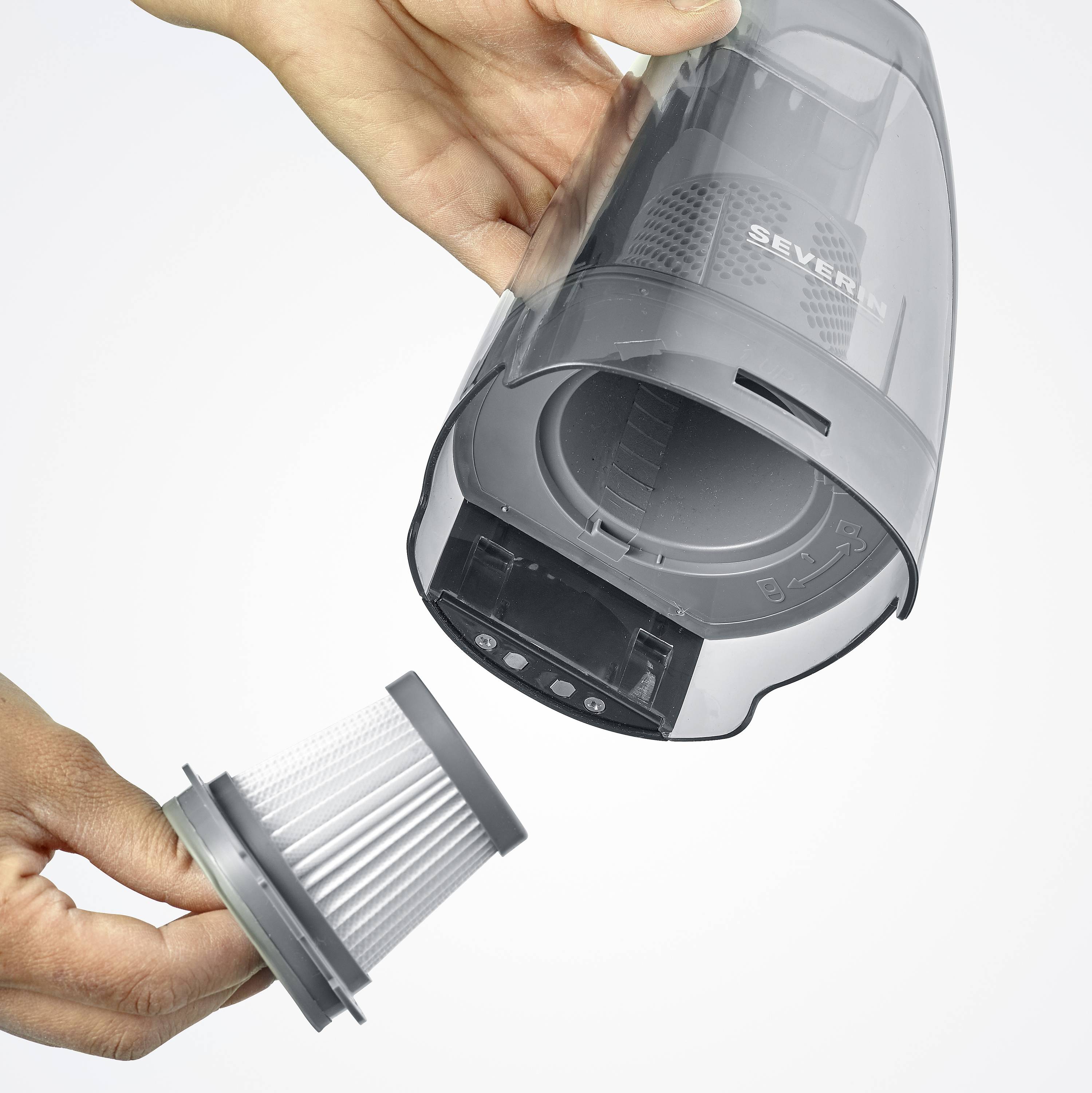 Eine Person zeigt die Entnahme eines zylindrischen Staubfilters von einem grauen Handstaubsauger.