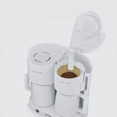 Eine weiße Kaffeemaschine mit offenem Deckel wird gezeigt, gefüllt mit Kaffeepulver in einem Filtereinsatz.