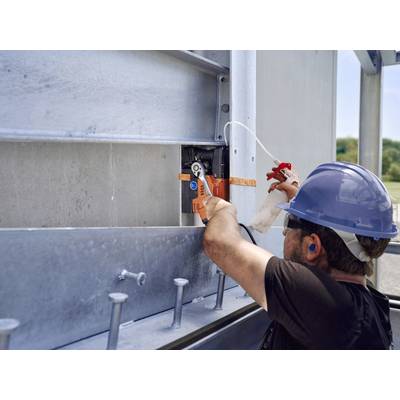 Ein Arbeiter mit Schutzhelm und Ohrstöpseln benutzt eine Zange, um an einer großen Metallstruktur zu arbeiten.