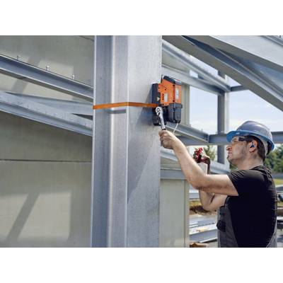 Ein Bauarbeiter mit Helm befestigt mit einem Schraubenschlüssel ein Stück Stahl an einer großen Stahlstütze einer Baustelle.