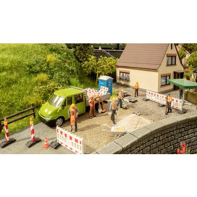 Mehrere Bauarbeiter in orangefarbener Arbeitskleidung arbeiten auf einer Baustelle vor einem Haus. Ein grünes Fahrzeug steht daneben.