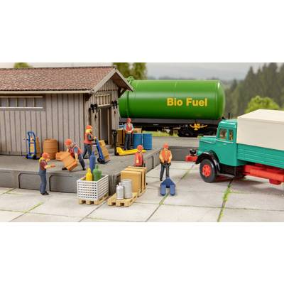 Figuren be- und entladen Fracht an einer Lagerhalle. Ein grüner Tank mit 'Bio Fuel'-Aufschrift steht im Hintergrund.
