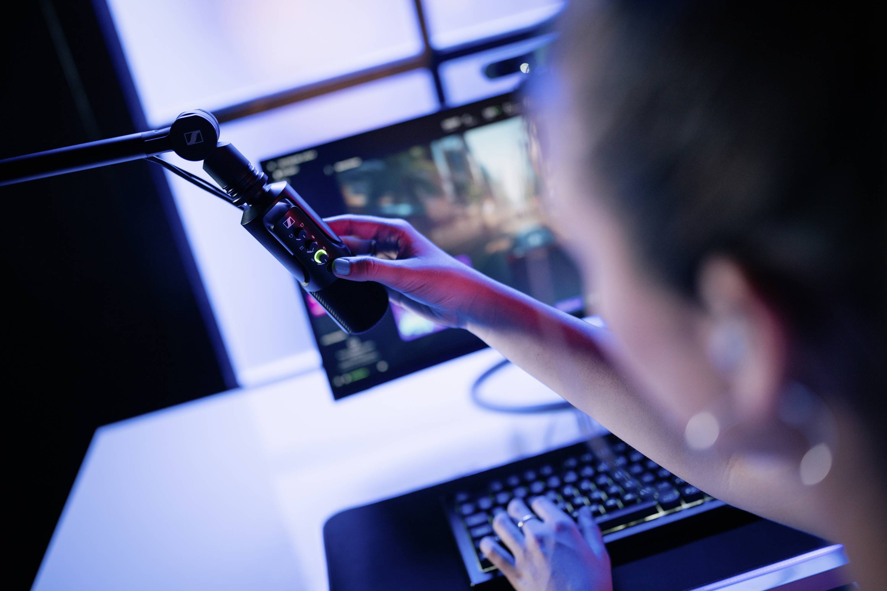 Eine Person bedient ein Mikrofon vor einem Computerbildschirm, offenbar während einer Aufnahme oder eines Livestreams.