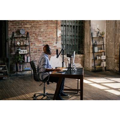 Eine Person sitzt an einem Schreibtisch in einem industriell gestalteten Raum, arbeitet am Computer und trägt Kopfhörer. Holzfußboden und Ziegelwände.
