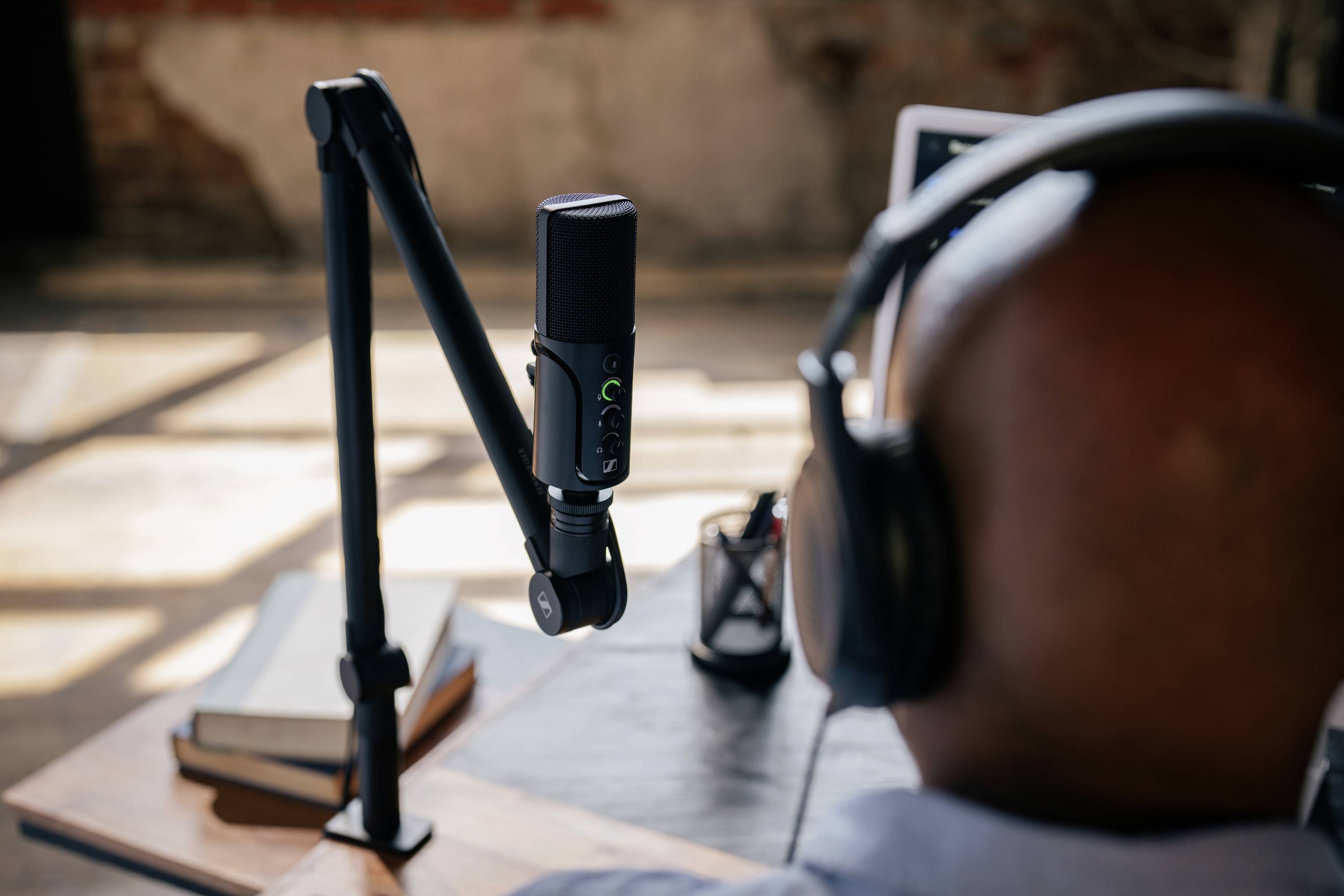 Ein Mann mit Kopfhörern sitzt an einem Tisch mit einem Mikrofon, konzentriert auf das, was er aufnimmt oder spricht.