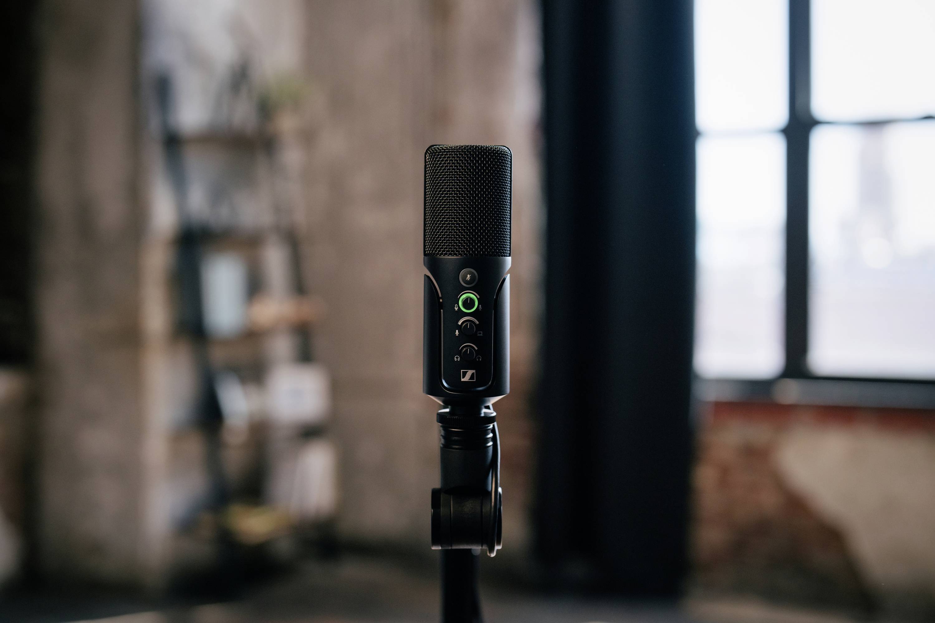 Ein schwarzes Mikrofon steht in einem Raum mit industriellem Design. Im Hintergrund sind ein Regal und ein Fenster zu sehen.