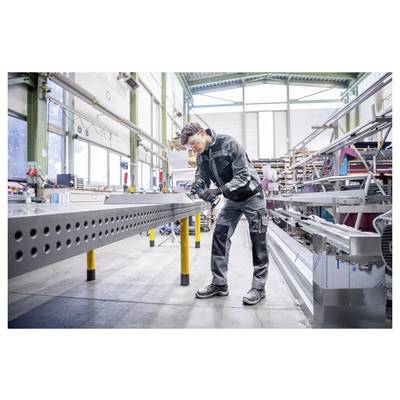 Arbeiter in Schutzausrüstung verwendet ein tragbares Werkzeug zur Inspektion oder Montage eines großen Metallbalkens in einer Industriefabrik.