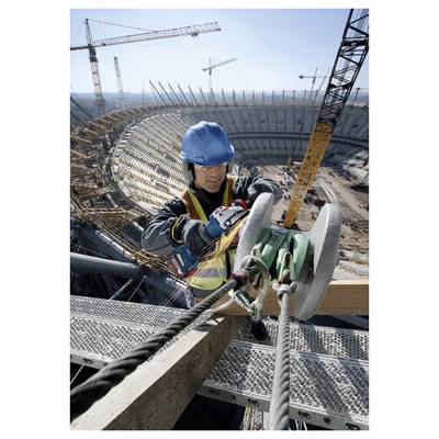 Ein Bauarbeiter in Sicherheitsausrüstung befestigt Seile an einem Metallträger auf einer Baustelle eines großen Stadions, umgeben von Kränen und Ausrüstung.