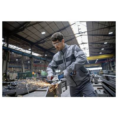 Ein Mann in Schutzausrüstung benutzt eine Winkelschleifer an Metall in einer großen Industriehalle, während Funken beim Kontakt sprühen.