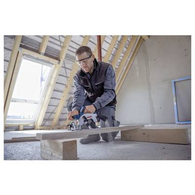 Eine Person mit Schutzbrille verwendet eine Kreissäge, um ein Holzbrett in einem unfertig ausgebauten Dachboden zu schneiden, während Licht durch ein Fenster fällt.