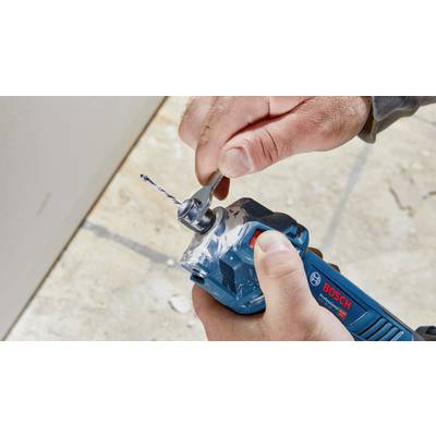 Eine Person hält eine blaue Bohrmaschine und befestigt einen Bohrer mit einem Schraubenschlüssel. Die Szene zeigt Handwerksarbeit.