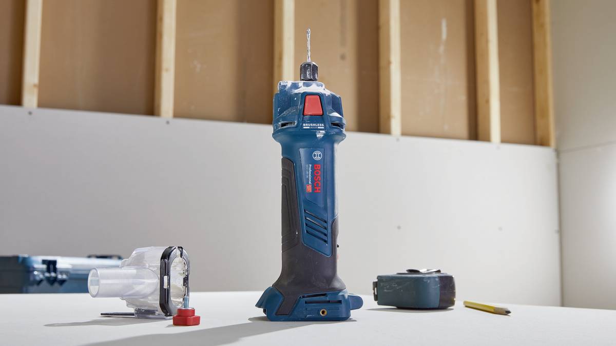 Ein blaues Elektrowerkzeug steht auf einem Tisch, umgeben von einer Plastikabdeckung, einem Maßband und einem Stift; Innenraum einer Baustelle.