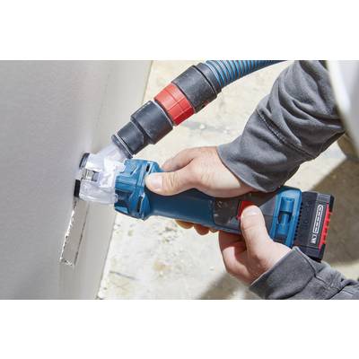 Eine Person benutzt ein blaues, elektrisches Multifunktionswerkzeug mit einem Staubsaugeraufsatz, um ein rechteckiges Loch in eine Wand zu schneiden.