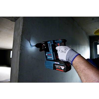 Eine Person bohrt mit einem blauen Akkubohrhammer ein Loch in eine Betonwand. Sie trägt dabei Arbeitshandschuhe.