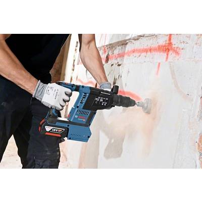 Person arbeitet mit einem elektrischen Bohrhammer, bohrt ein Loch in eine Betonwand, trägt Schutzbekleidung. Baustellenumgebung.