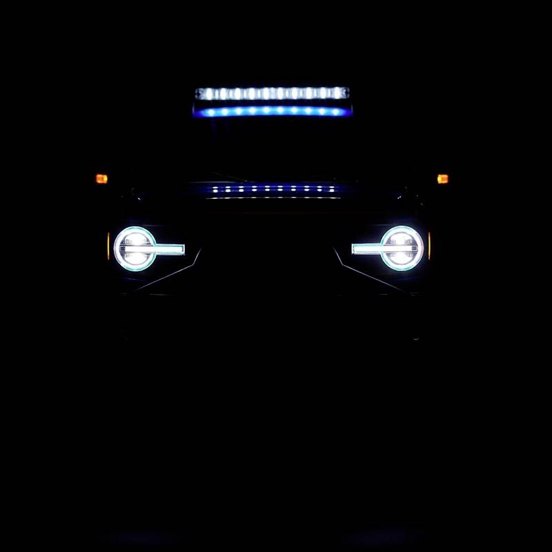 Ein Auto mit eingeschalteten Scheinwerfern und einer Lichtleiste ist stark abgedunkelt und erscheint vor einem schwarzen Hintergrund.