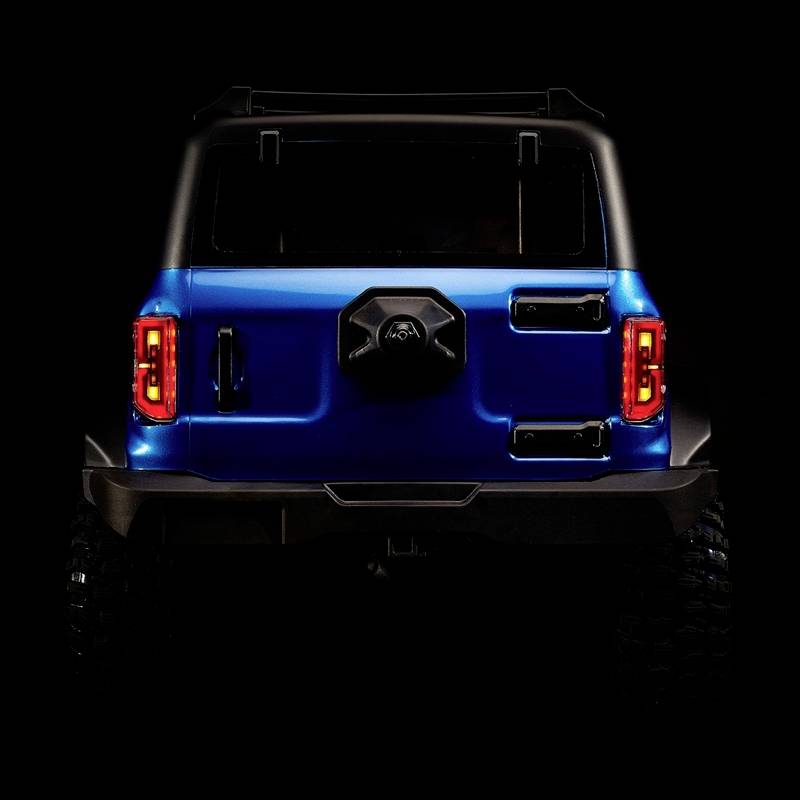 Ein blauer Geländewagen von hinten, beleuchtet auf schwarzem Hintergrund, zeigt robuste Bauweise und markante Rücklichter.