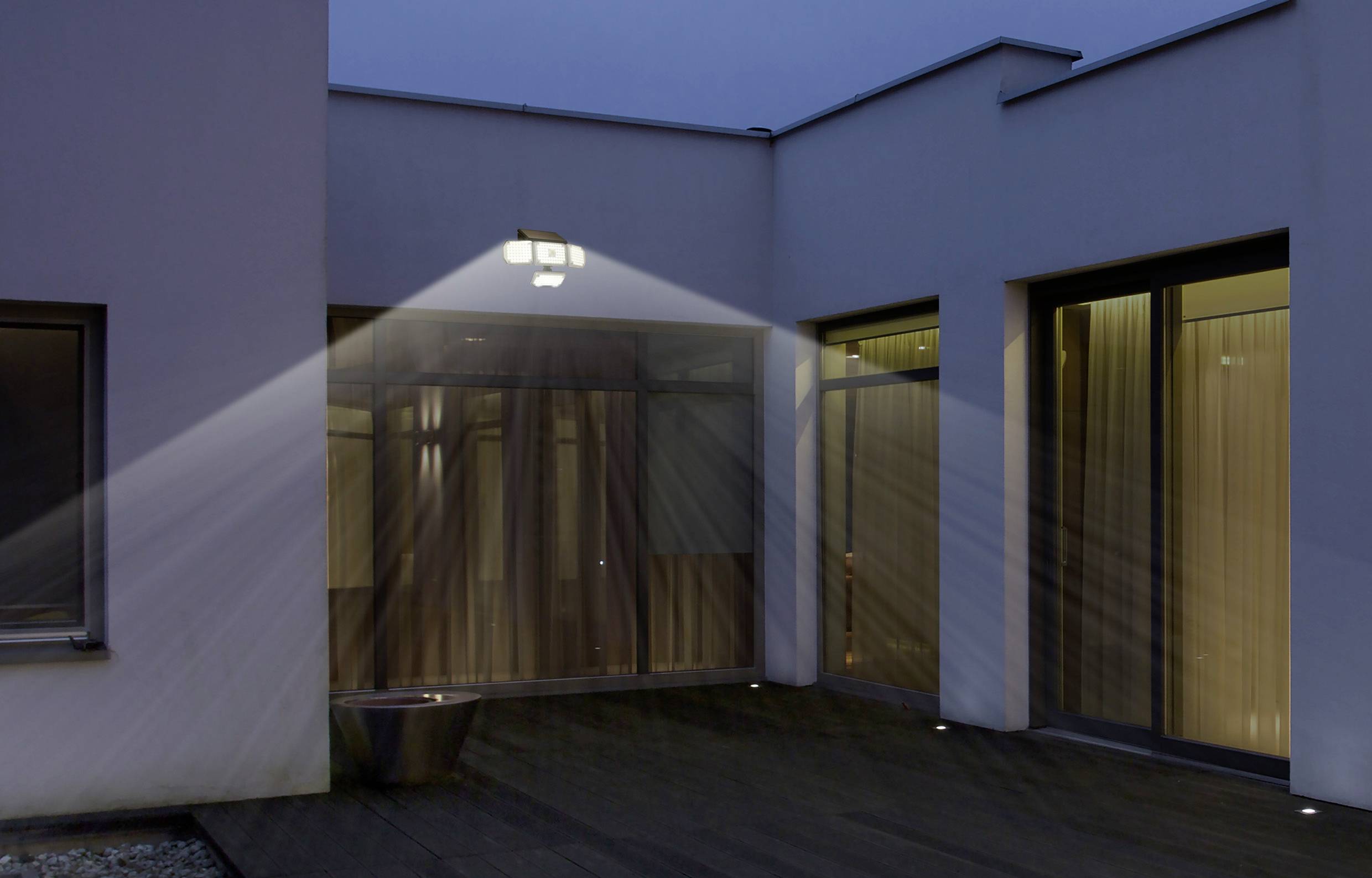 Außenleuchte beleuchtet den Eingang eines modernen Gebäudes bei Abenddämmerung, erzeugt gleichmäßig verteilt Lichtkegel.