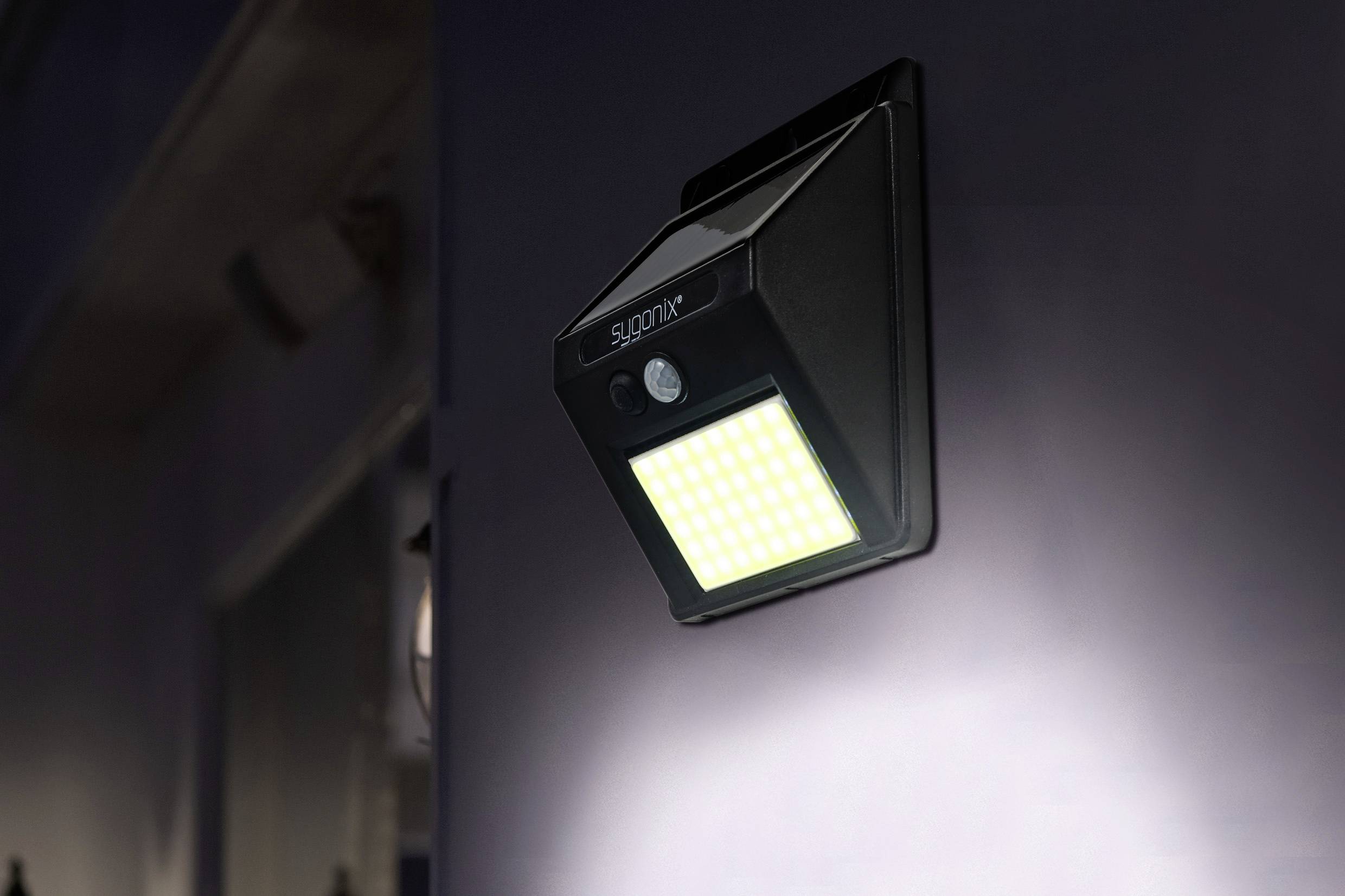 Ein schwarzes, solarbetriebenes LED-Licht ist an einer Wand montiert. Es leuchtet hell, ideal zur Beleuchtung von Außenbereichen.
