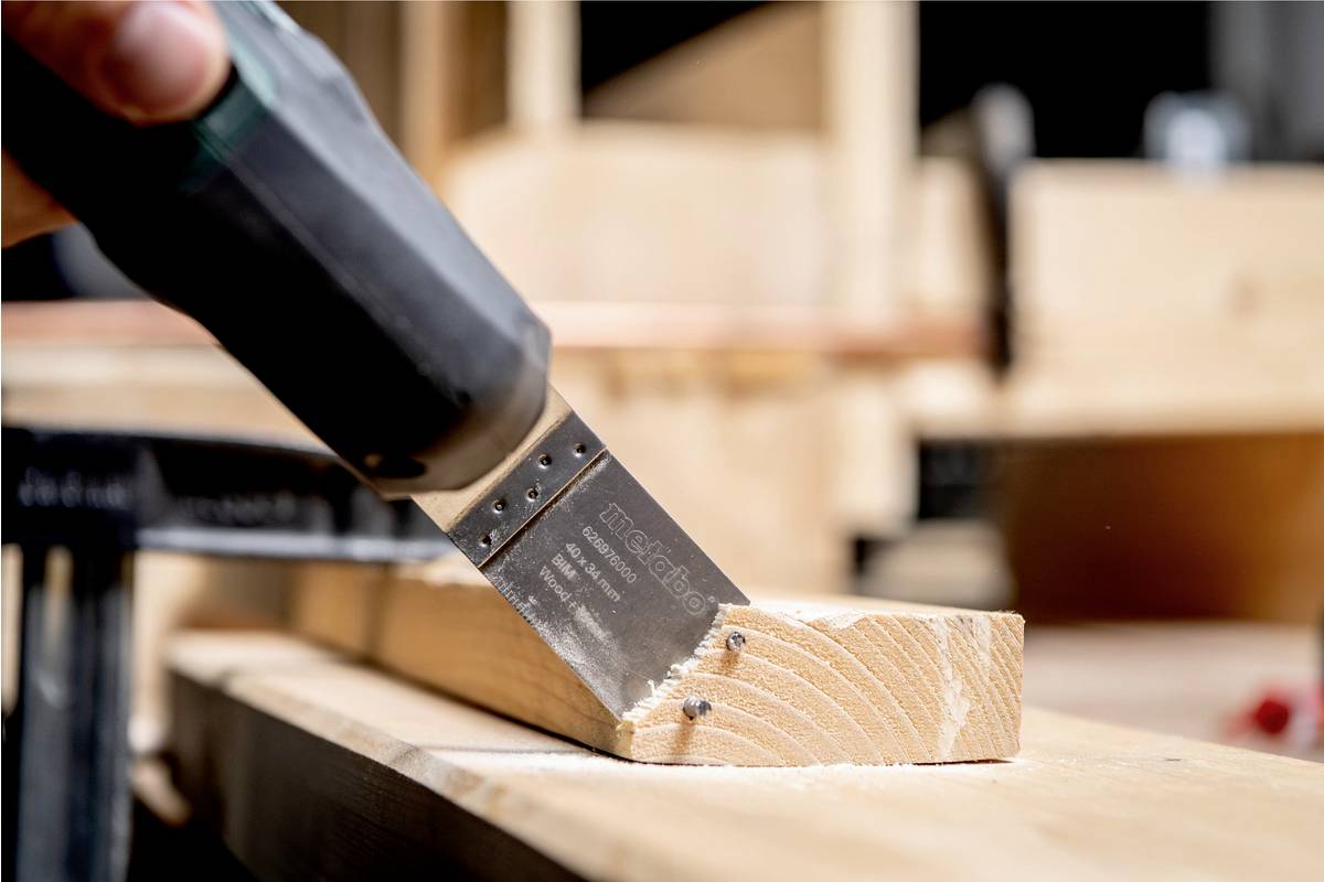 Eine Hand hält eine Säge und schneidet präzise ein Holzbrett in einer Werkstattumgebung.