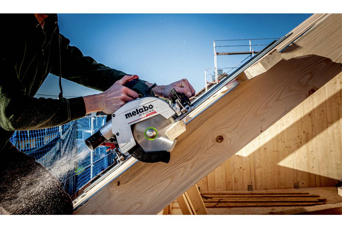 Person schneidet Holz mit einer Kreissäge auf einer Baustelle. Es ist sonnig und man sieht ein Gerüst im Hintergrund.