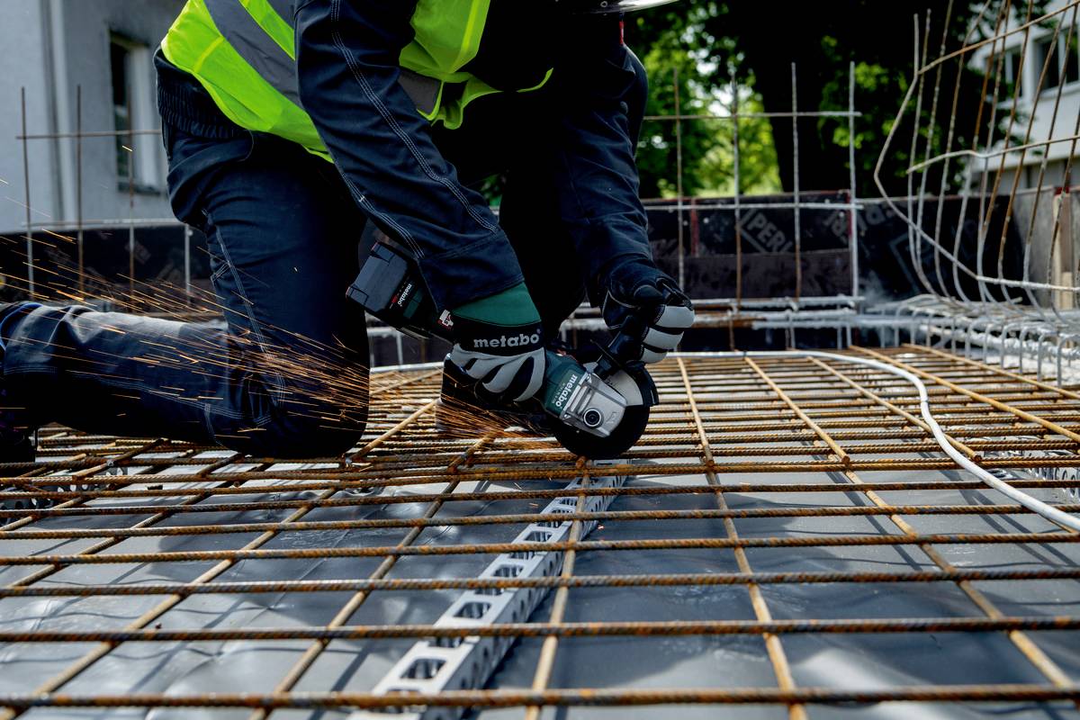 Ein Bauarbeiter schneidet mit einem Winkelschleifer Stahlgitter auf einer Baustelle. Funken fliegen von der Schleifscheibe.