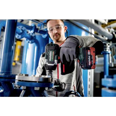 Ein Arbeiter in Schutzbrille und Handschuhen befestigt ein Metallteil mit einem Metabo-Akkuschrauber in einer industriellen Umgebung.