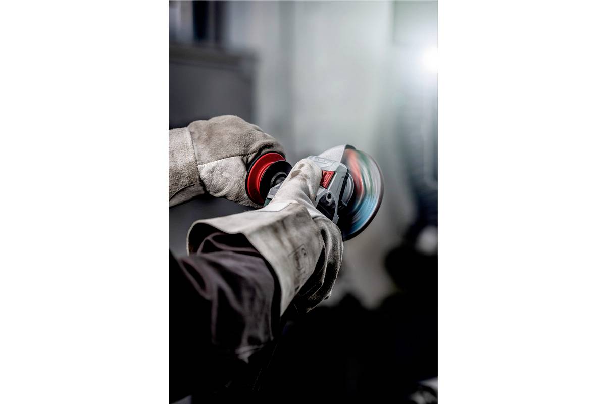 Eine Person trägt Handschuhe und verwendet ein Elektrowerkzeug. Der Hintergrund ist unscharf, was auf einen konzentrierten Arbeitsvorgang hindeutet.