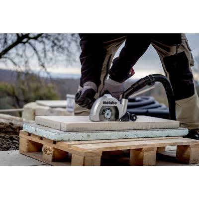 Eine Person schneidet mit einer elektrischen Säge eine Fliese auf einer Baustelle. Die Fliese liegt auf einer Palette im Freien.