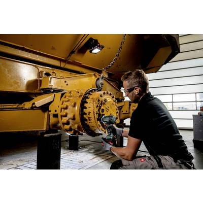 Eine Person repariert mit einem elektrischen Schraubenzieher das Rad einer großen gelben Maschine in einer Werkstatt.