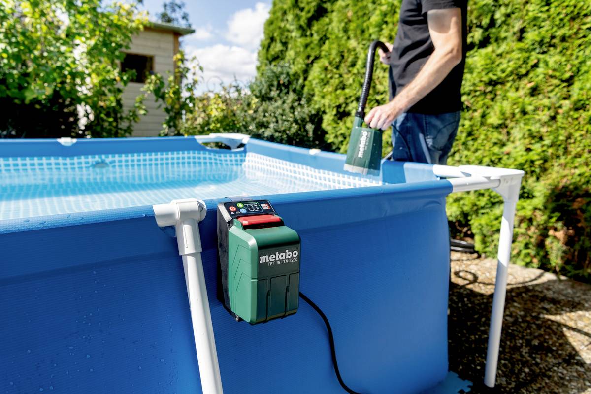 Ein Mann benutzt eine elektrische Pumpe, um einen Aufstellpool zu leeren. Eine Metabo-Pumpe ist an der Seite des Pools befestigt.